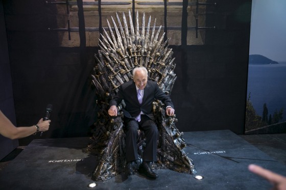 Former Israeli president Peres smiles as he sits on the Iron Throne during the opening of the Game of Throne exhibition in Tel Aviv